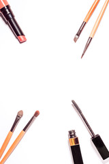 Flat lay with make up products in minimal style on white desk. Frame with black mascara, lipstick, spring eyeshadow palette, different make up brushes. Top view, copy space.