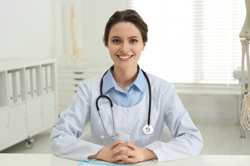 Female orthopedist at table near human skeleton model in office