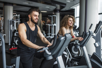 Fototapeta na wymiar Attractive young woman and her trainer running on treadmill in gym. Slim girl jogging in fitness club, smiling at camera. Healthy lifestyle concept, cardio training