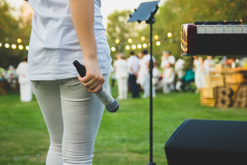 A slender woman in white clothes with a microphone in her hand stands on the background of people.