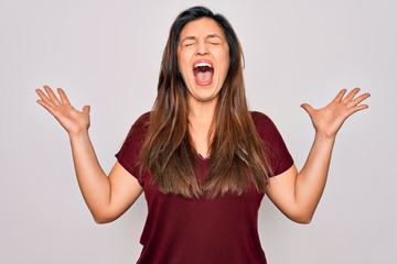 Young hispanic woman wearing casual t-shirt standing over isolated background celebrating mad and crazy for success with arms raised and closed eyes screaming excited. Winner concept