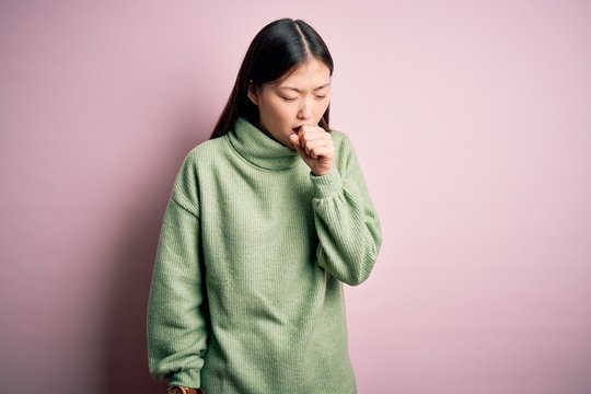 Young beautiful asian woman wearing green winter sweater over pink solated background feeling unwell and coughing as symptom for cold or bronchitis. Health care concept.