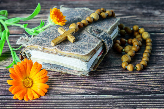 Wooden cross with beads on the ancient bible on the wooden background. Christian religion concept.