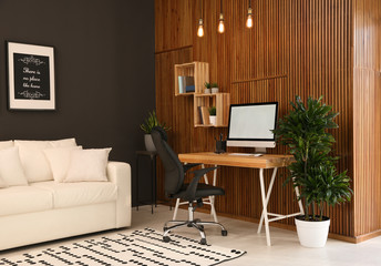 Obraz premium Comfortable workplace with computer near wooden wall in stylish room interior. Home office design