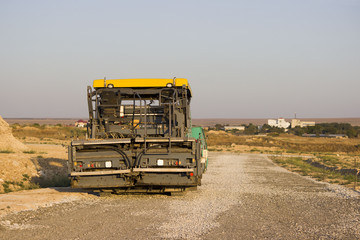 gravel and asphalt tamping machine stands on the road. road under construction. Gravel poured in the steppe as a substrate in front of asphalt