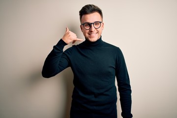 Young handsome caucasian man wearing glasses and casual sweater over isolated background smiling doing phone gesture with hand and fingers like talking on the telephone. Communicating concepts.