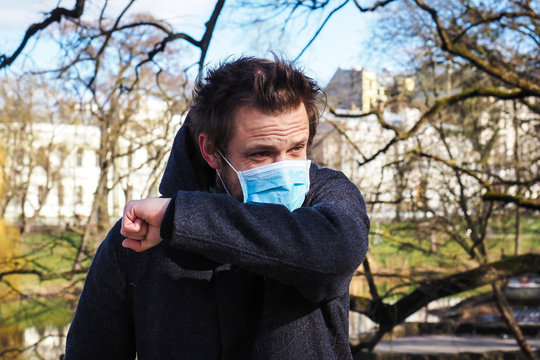 Handsome young European man coughing on the street with a medical face mask on. Closeup of a 35-year-old male in a respirator to protect against infection with influenza or coronavirus (Covid-19)