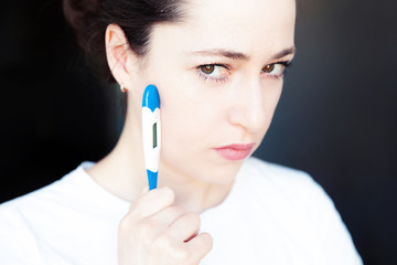 Young woman holding medicine equipment thermometer isolated on dark black background. Ill girl...