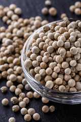 white peppercorns in glass bowl on stone background