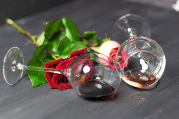 Pair of glasses with red and pink wine laying on black wooden background, rose flowers