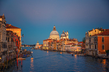 Venice cityscape with Grand Canal waterway. Buildings with evening lights along Grand Canal. Santa Maria della Salute Roman Catholic church on Punta della Dogana at twilight. Veneto Region, Italy.