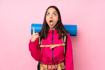 Young mountaineer girl with a big backpack over isolated pink background pointing up and surprised