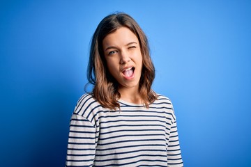 Fototapeta premium Young beautiful blonde girl wearing casual sweater standing over blue isolated background winking looking at the camera with sexy expression, cheerful and happy face.