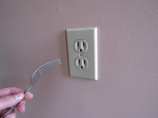 A person putting a fork into an electrical outlet 