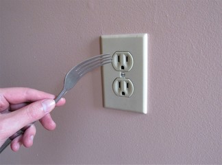 A person putting a fork into an electrical outlet 