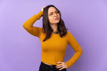 Young mixed race woman isolated on purple background having doubts while scratching head