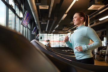Side view portrait of sportive young woman running on treadmill during cardio workout in modern gym, copy space