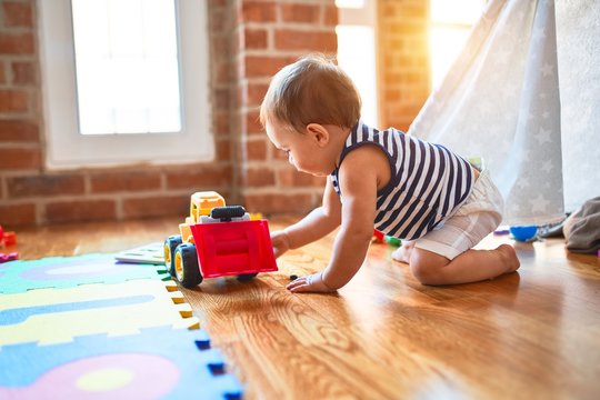 Adorable toddler crawling around lots of toys at kindergarten