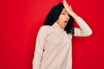 Young african american curly woman wearing casual turtleneck sweater over red background surprised...