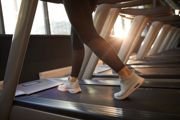 Low section portrait of sportive young woman running on treadmill during cardio workout in sunlit gym, copy space