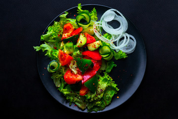 Fresh vegetables salad with purple cabbage, white cabbage, lettuce, carrot in dark clay bowl on black background. Top view