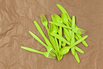 Biodegradable reusable recyclable green forks, spoons, knifes made from corn starch on brown crumpled craft paper. Eco, zero waste, alternative to plastic concept. Flat lay. Horizontal. Close-up
