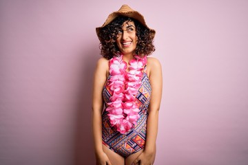 Young beautiful arab woman on vacation wearing swimsuit and hawaiian lei flowers looking away to side with smile on face, natural expression. Laughing confident.