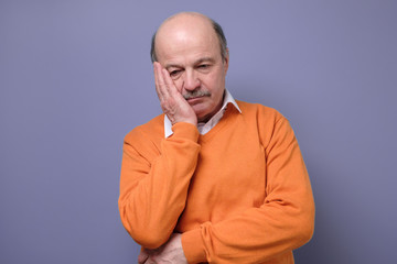 Sad mature hispanic man in orange sweater feeling stressed and alone.