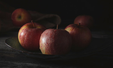 Still life of three red apples, on a wooden tray. Dark food