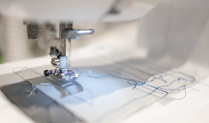 Close up view of sewing process. The stitching white fabric on professional manufacturing machine at workplace.