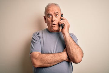 Middle age hoary man having conversation talking on the smartphone over white background scared in...