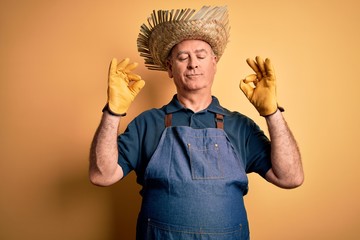 Middle age hoary farmer man wearing apron and hat over isolated yellow background relax and smiling with eyes closed doing meditation gesture with fingers. Yoga concept.