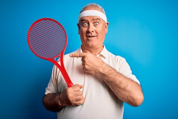 Middle age hoary sportsman playing tennis using racket over isolated blue background very happy pointing with hand and finger