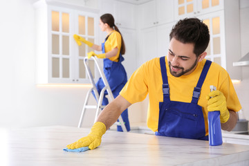 Professional young janitor cleaning table in kitchen
