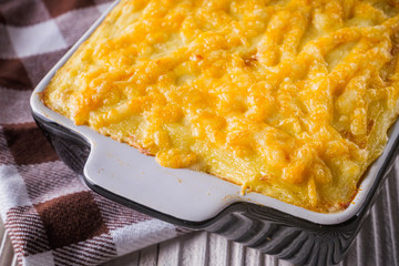 Delicious potato casserole with meat and cheese on a white wooden background