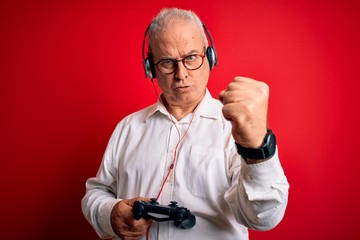 Middle age handsome hoary gamer man playing video game using joystick and headphones annoyed and frustrated shouting with anger, crazy and yelling with raised hand, anger concept