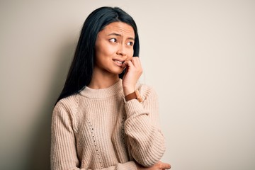 Young beautiful chinese woman wearing casual sweater over isolated white background looking stressed and nervous with hands on mouth biting nails. Anxiety problem.