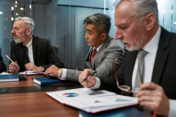 Discussing business. Multicultural business people in formal wear analyzing some documents and discussing project results while having a meeting in the office