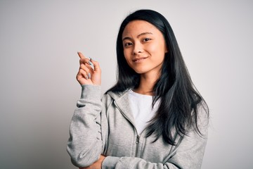 Young beautiful chinese sporty woman wearing sweatshirt over isolated white background with a big smile on face, pointing with hand and finger to the side looking at the camera.