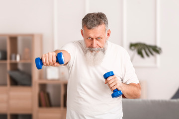 Sporty elderly man training with dumbbells at home