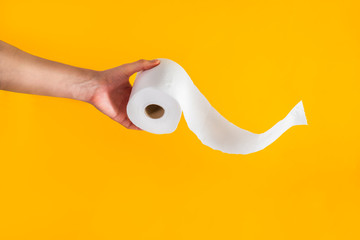 Close up caucasian male hand holding or giving a roll of toilet paper with flying tissue on bright yellow background. Crisis product lack concept. Copy space.