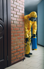 Pest control worker in protective suit spraying pesticide indoors