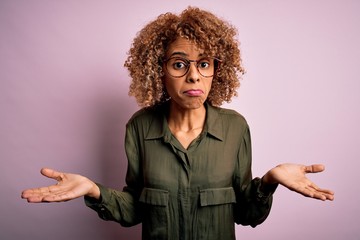 Young beautiful african american woman wearing casual shirt and glasses over pink background...