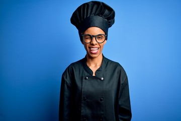 Young african american chef woman wearing cooker uniform and hat over blue background winking looking at the camera with sexy expression, cheerful and happy face.