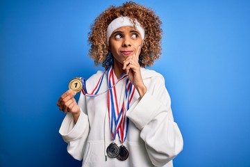 Young african american sporty woman with curly hair doing sport winning medals serious face...