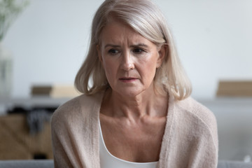 Head shot close up portrait unhappy older female retiree sitting alone, trying remember important event or information. Frustrated worrying middle aged sad woman having problem with memory or health.