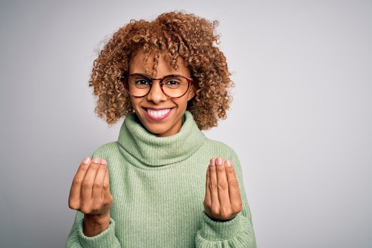 Young beautiful african american woman wearing turtleneck sweater and glasses doing money gesture with hands, asking for salary payment, millionaire business