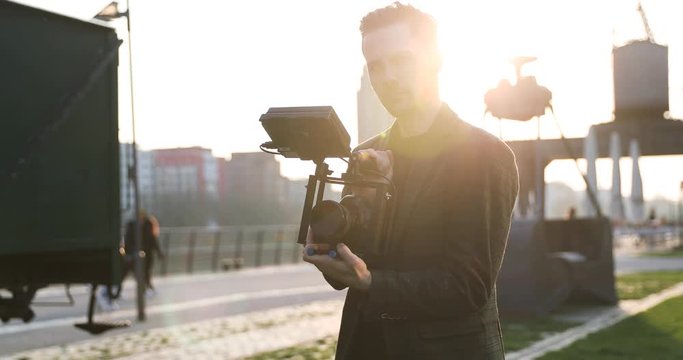 Male Filmmaker smile on to the camera on sunset in a big city. Industrial