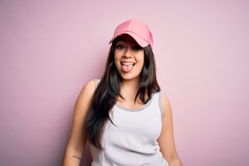 Fototapeta premium Young brunette woman wearing casual sport cap over pink background sticking tongue out happy with funny expression. Emotion concept.