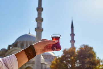 A cup (armud) of traditional Turkish tea in hand against the background of a mosque in Istanbul